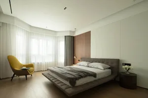 A modern bedroom featuring a sleek bed with a floating bedside table and a yellow accent chair.