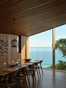 Modern minimalist dining room featuring a long wooden table and chairs with a view of the ocean.