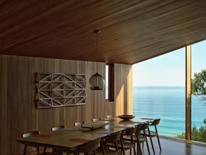 Modern minimalist living room with expansive wooden walls and floor, large windows overlooking the ocean, and a long wooden d