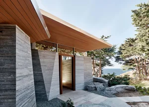 A modern residential exterior featuring stone walls and glass elements against a serene coastal backdrop.
