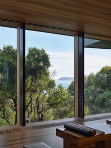Modern residential window view featuring a blend of wood and glass materials, providing a serene coastal and forest backdrop.