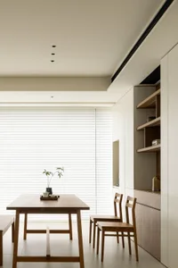 Minimalist dining room featuring a wooden table and chairs with a simple plant centerpiece, against a large window with white