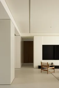 A minimalist living room featuring concrete walls and flooring, with a wooden chair and black television setup.