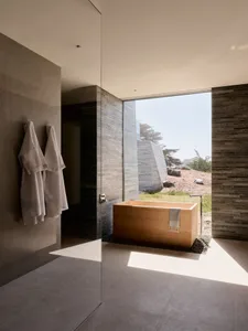 A modern bathroom featuring a wooden bathtub surrounded by concrete tiles and natural light.