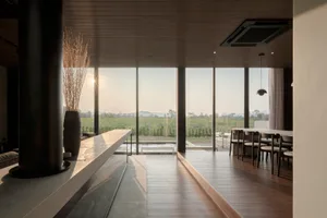 A modern dining room featuring a glass wall and minimalist furniture, providing a serene view of the landscape outside.
