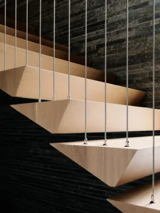 Modern floating staircase with wooden steps hanging by metal cables against a dark brick wall