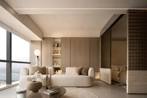 Modern living room featuring beige-colored sofas with brown and beige cushions, a round glass coffee table with a vase of flo