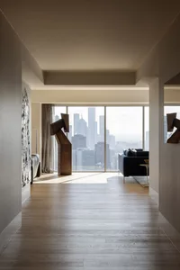 Interior view of a modern living room featuring a wood floor and a cityscape view through large windows.