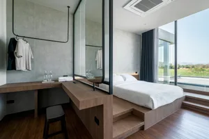 Modern minimalist bedroom with white bedding, dark wood flooring, and large windows showing a scenic view.