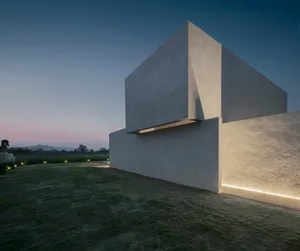 A modern minimalist house with a concrete exterior illuminated at dusk.