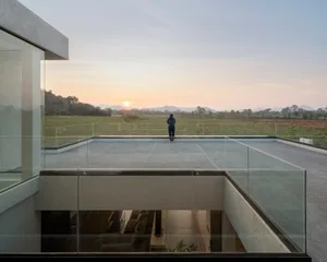 A modern residential building featuring glass walls overlooking a scenic landscape at sunset.