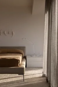 Modern minimalist bedroom featuring a grey fabric bed, a white floating nightstand, and sheer curtains allowing soft light to