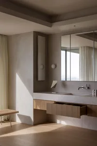Modern minimalist bathroom featuring a white ceramic vanity, wooden drawers, and metallic fixtures against a textured ceramic