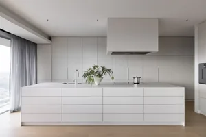 Modern minimalist kitchen with white cabinets, stainless steel appliances, and a large island.