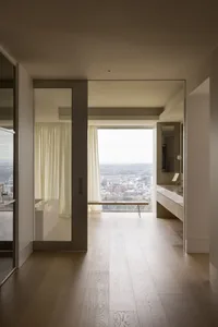 A minimalist residential interior with wooden floors, glass walls, and white porcelain fixtures.