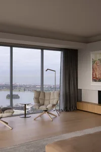 Contemporary living room featuring large windows overlooking a cityscape with wooden flooring, plush seating, and minimalist 