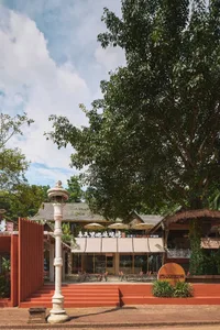 A restaurant exterior made of brick and wood with white parasols and green trees in the background.