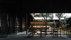 Modern restaurant courtyard with wooden tables, glass walls, and stone elements.
