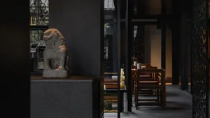 A modern restaurant interior featuring a stone lion statue and dark furnishings.