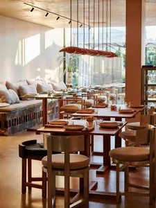 Modern restaurant interior with wooden tables, cushioned chairs, and warm lighting.