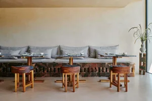 A stone and wood restaurant interior with cushioned seating, tables, and stools.