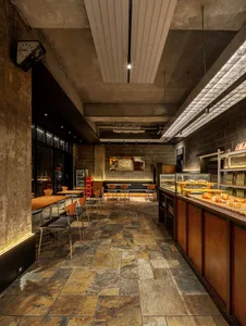 Industrial-style cafe interior with concrete walls, stone flooring, and wooden furniture.