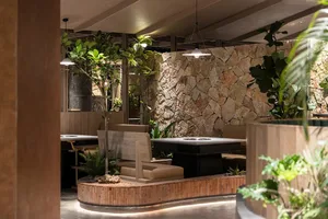A view of a restaurant interior featuring stone walls, concrete seating, and indoor plants.
