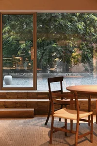 Modern cafe interior with a window view showcasing a wooden table and chairs surrounded by lush green foliage, with a white c