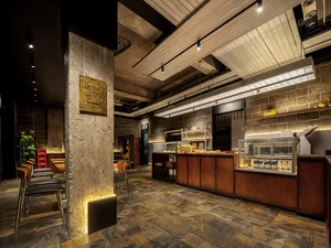 An industrial-style restaurant interior featuring concrete floors, brick walls, and wooden accents.