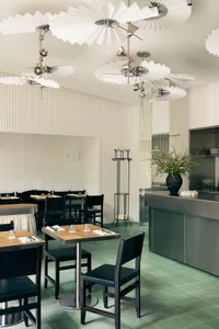 Modern restaurant interior with minimalist lighting, white ceiling fans, and green tiled floor.