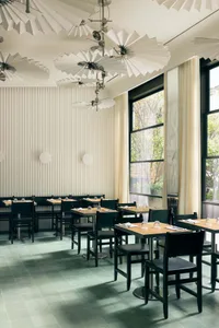 A modern restaurant with minimalist decor, featuring tables made of wood and metal, and glass elements.