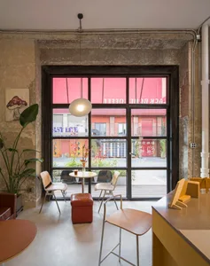 An industrial-style cafe interior with concrete walls, large glass windows, and seating arrangements