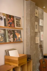 A music room with concrete walls, a wooden shelf displaying vinyl records, and a guitar leaning against the wall.