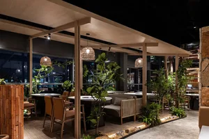 Industrial restaurant interior with concrete and wood materials, natural-fiber pendant lights, and green plants.