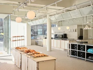 A minimalist bakery interior with concrete and glass elements showcasing a variety of bread items on display.