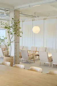 A minimalist coffee shop with concrete walls, wooden furniture, and white fabric seating.