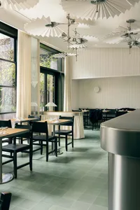 Modern restaurant interior with glass ceiling fans, wood tables, and metal bar counter.