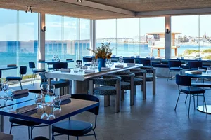 Modern restaurant interior with glass walls and tables overlooking the ocean.
