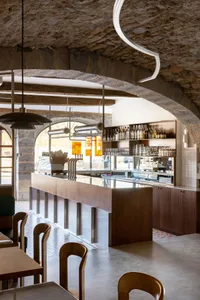 A minimalist café interior featuring wooden furniture, stone ceiling, and glass displays.