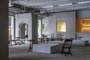 A modern cafe interior with concrete flooring, minimalist furniture, and a gold-framed mirror.