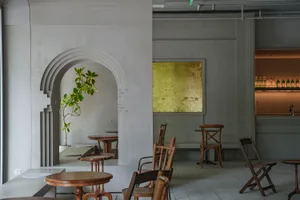 A modern cafe interior featuring a concrete wall with an arch and a gold-framed wall art.
