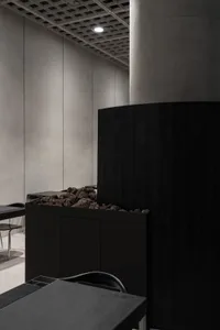 Industrial-style restaurant interior with concrete walls and floor, featuring a dark wood panel and rock garden.