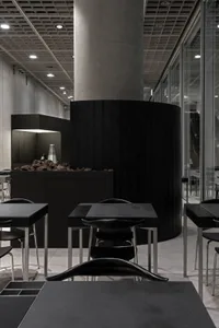 Modern minimalist interior of a coffee shop with black tables, chairs, and wood paneling.