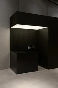 A minimalist black reception counter with a metallic finish, illuminated by a sleek overhead light fixture.