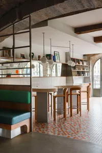 A modern restaurant bar with concrete walls, wooden stools, and tiled floor