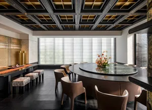 A modern dining room with a round marble table and leather chairs, featuring a floral centerpiece and a coffered ceiling.