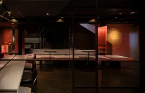 Modern restaurant interior with concrete finishes, glass partitions, and wooden seating.