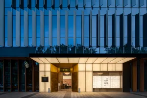A modern retail storefront illuminated by stylish lighting, featuring metallic and glass panels with stone accents.