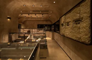 Interior of an artisan bakery with stone walls, concrete flooring, and glass display cases.