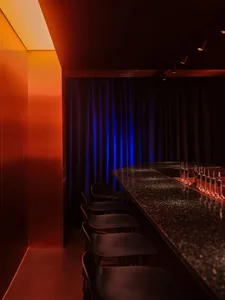 A sleek, metallic bar interior with black accents and a drink station featuring various bottles.